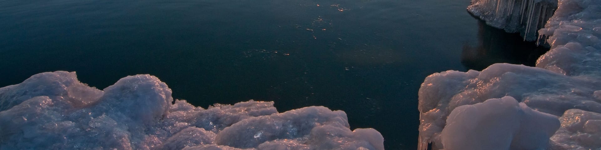 The sun rises over ice formations on the Lake Michigan shoreline on a peaceful winter morning.
