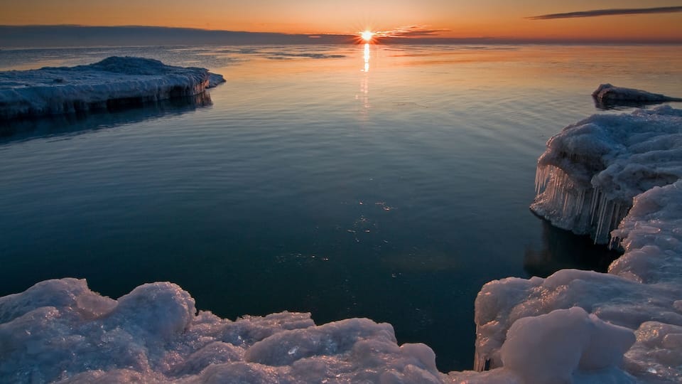 A frozen lake at sunset with ice formations and a clear sky.