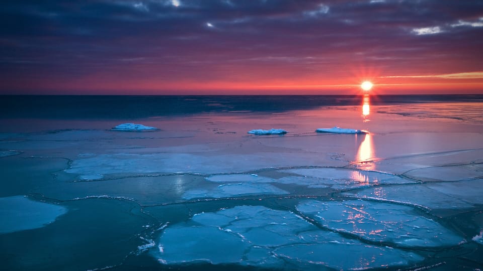 A sunset over a frozen lake with icebergs.