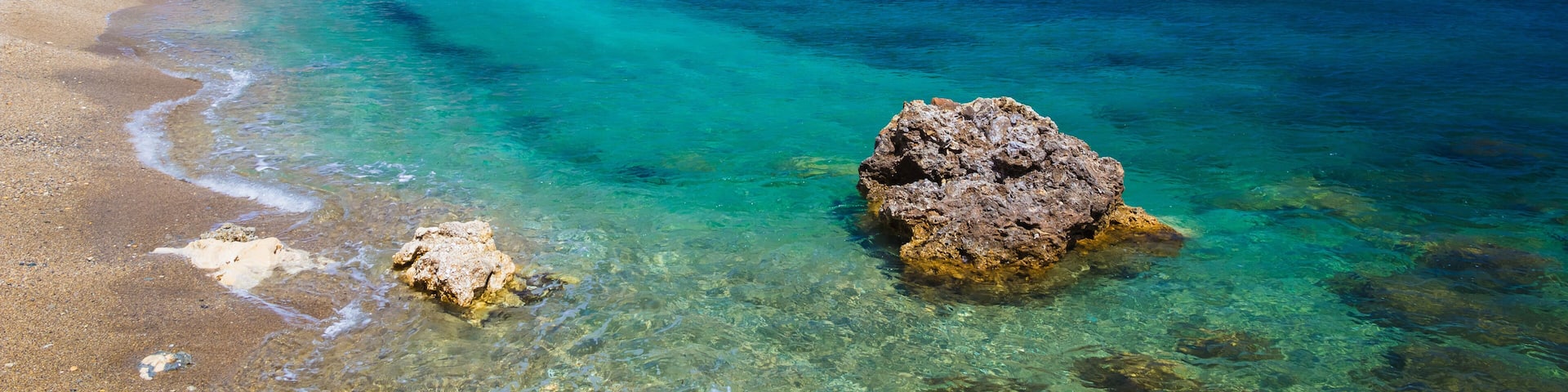 A coastal landscape with clear turquoise waters, rocky cliffs, and a sandy beach.