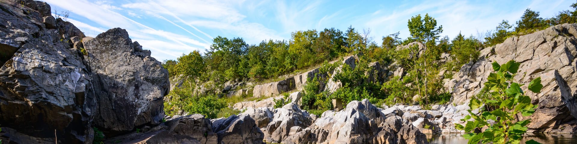 A rocky landscape with a clear pond surrounded by greenery and trees.