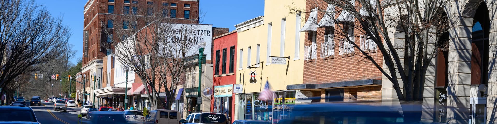 A busy urban street lined with various buildings, including a red brick building and a yellow building with a sign that reads 'evaluate.'