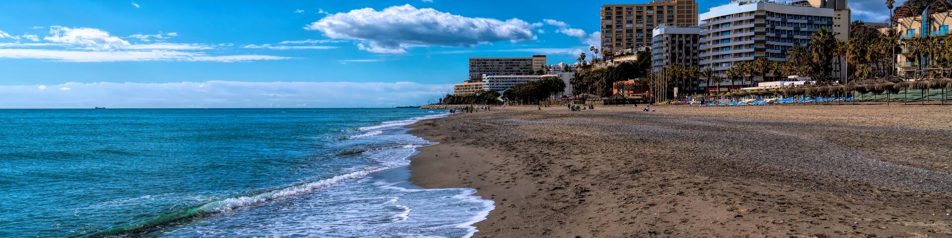 A beach with waves, a clear sky, and buildings in the background.