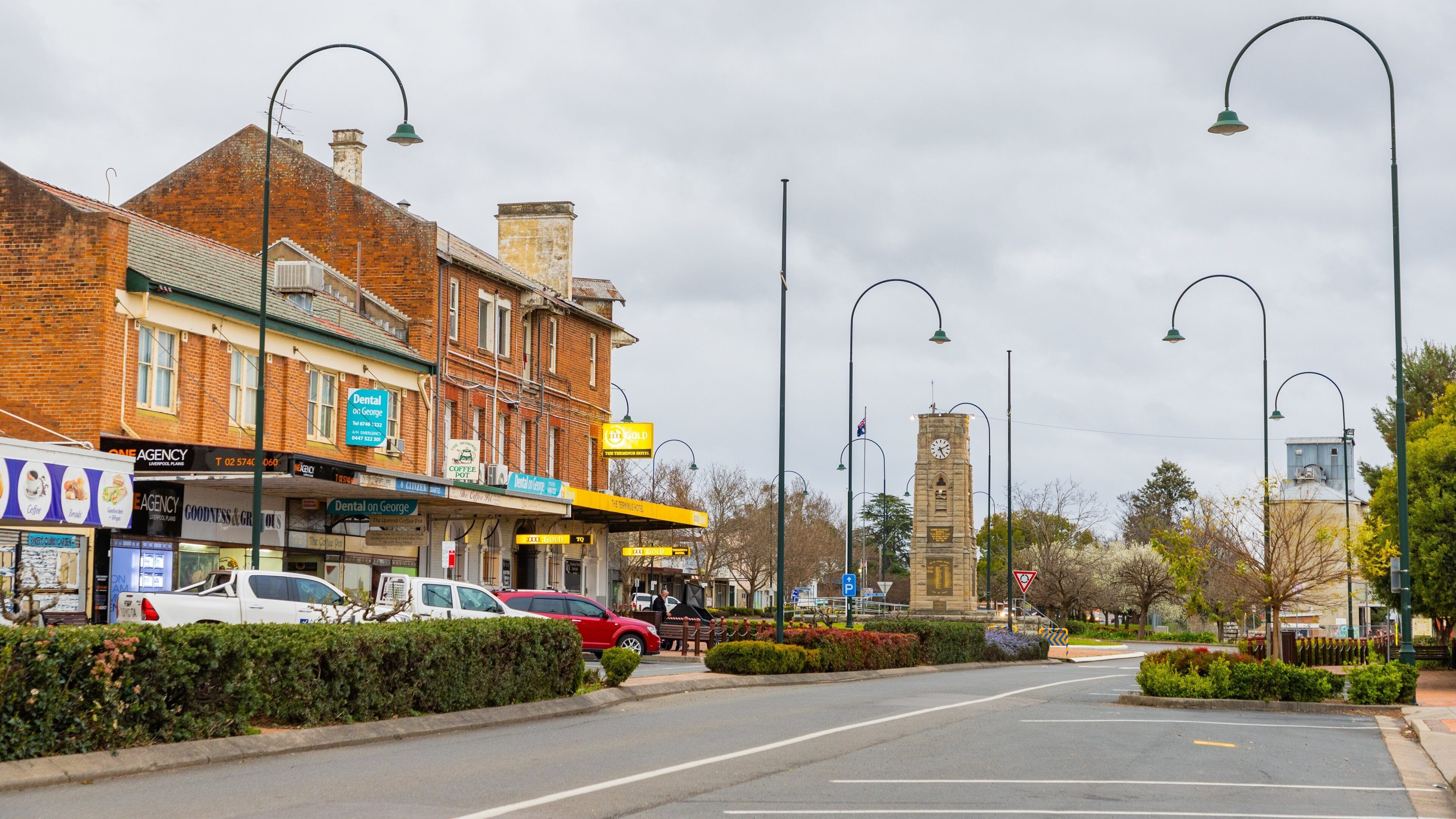 A street with brick buildings, parked cars, and a clock tower.