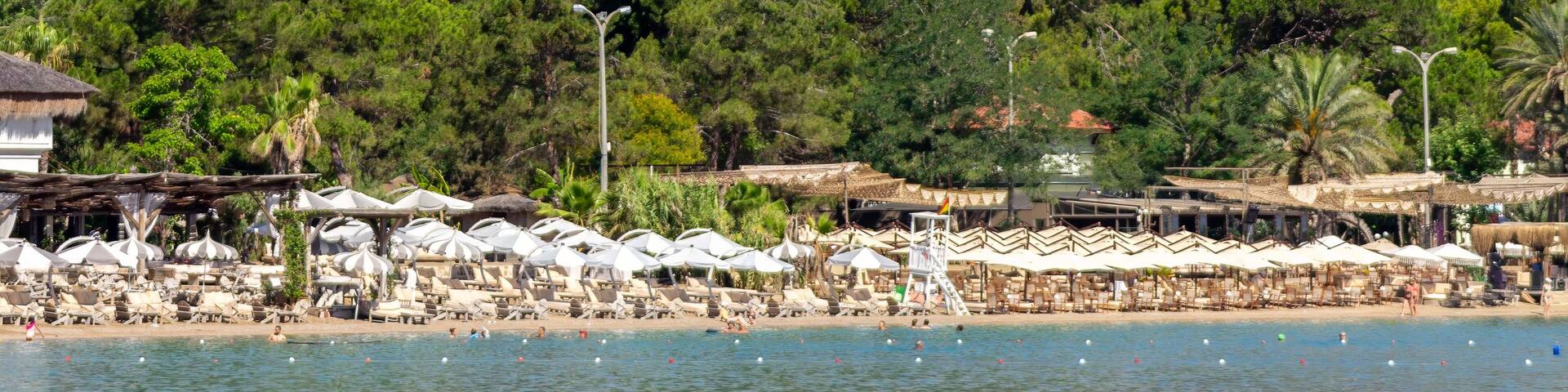 A beach with umbrellas and lounge chairs, a lifeguard tower, and a mountainous backdrop.