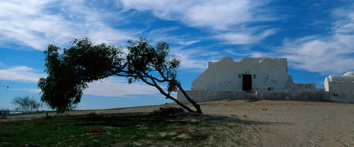 A white building with a dome and a door, surrounded by a barren landscape and a clear sky.