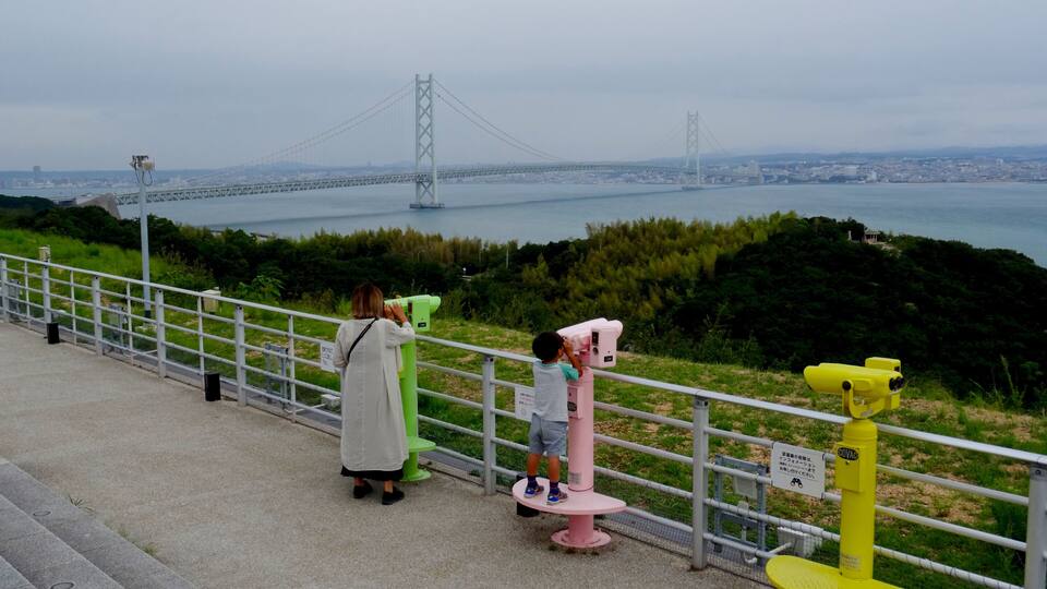 A coastal overlook with a bridge in the distance, a railing, and binoculars for viewing.