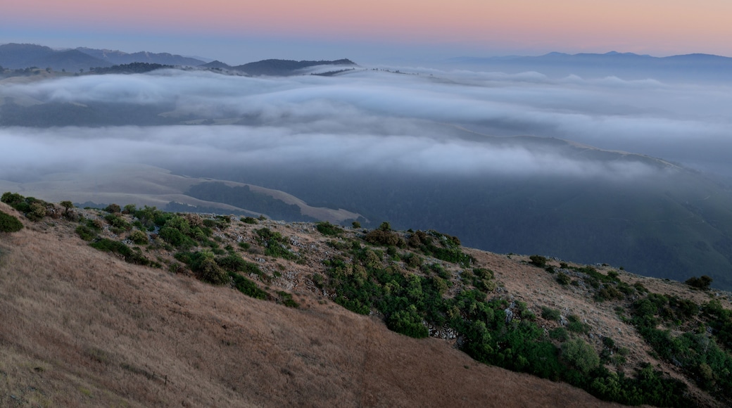 Paisaje montañoso con colinas ondulantes, una densa niebla y un cielo despejado.