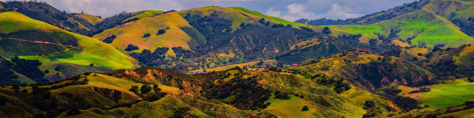Rolling green hills with a valley and a cloudy sky.