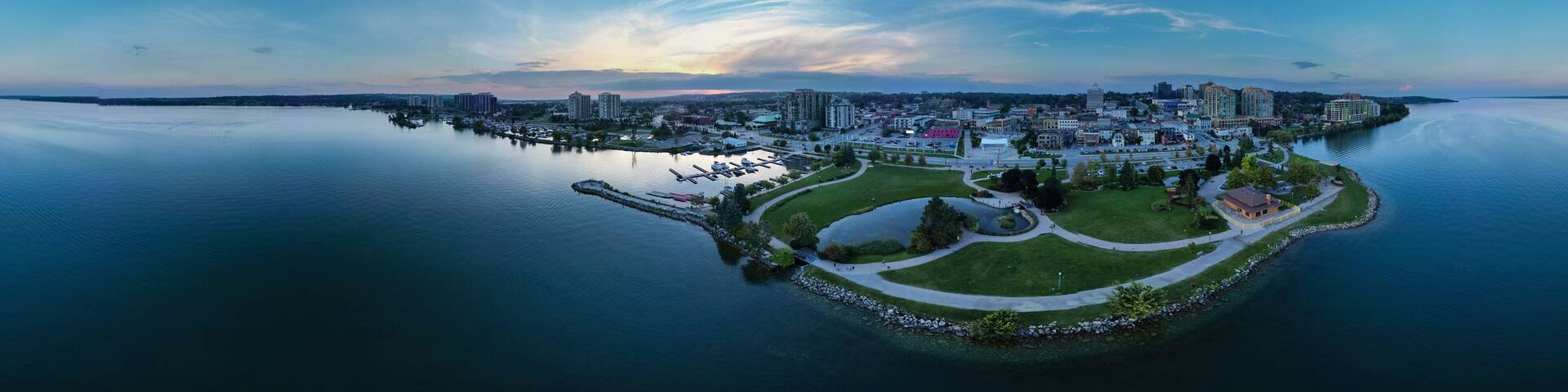 A coastal cityscape with a large body of water, a park with a circular walking path, and various buildings.