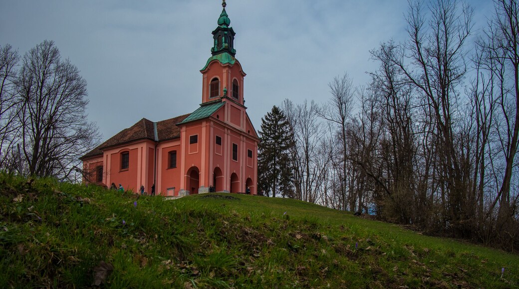 Red church with green copper roof on the top of the Roznik hill in Ljubljana slovenia on a cloudy day in early spring.