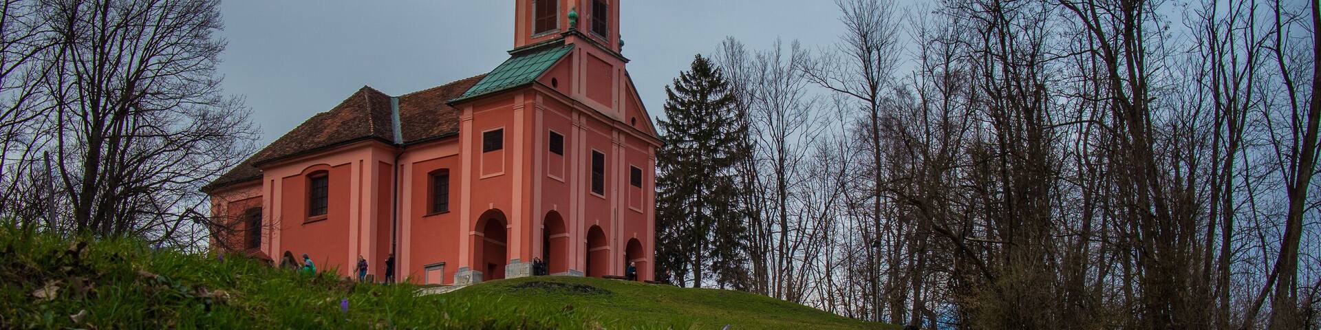Red church with green copper roof on the top of the Roznik hill in Ljubljana slovenia on a cloudy day in early spring.