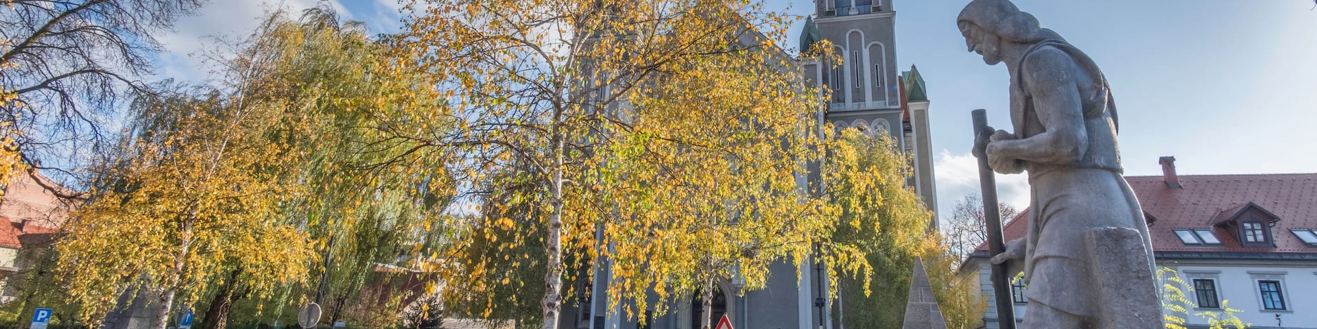 A church with a clock tower, autumn leaves, and a statue.