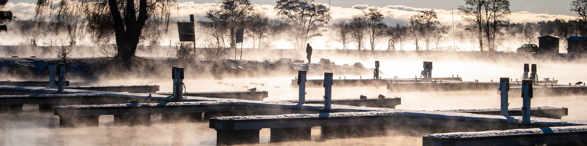 A misty lakeside with wooden docks and leafless trees.