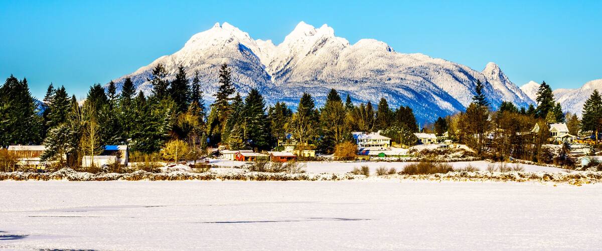 Un paysage enneigé, avec une chaîne de montagnes en arrière-plan et un groupe de maisons au premier plan.