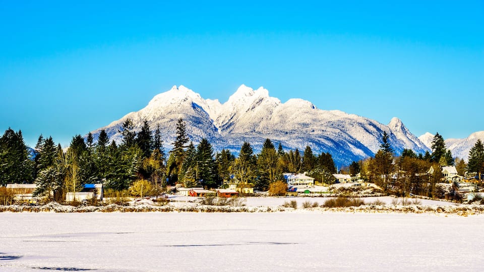 The snow covered peaks of the Golden Ears mountain behind the town of Fort Langley in the Fraser Valley of British Columbia, Canada on a cold winter day and snow covered fields under clear blue sky