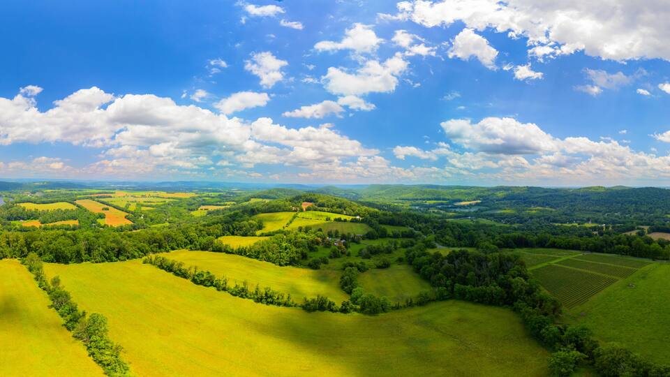 Rolling green hills, a river, and a clear blue sky with clouds.