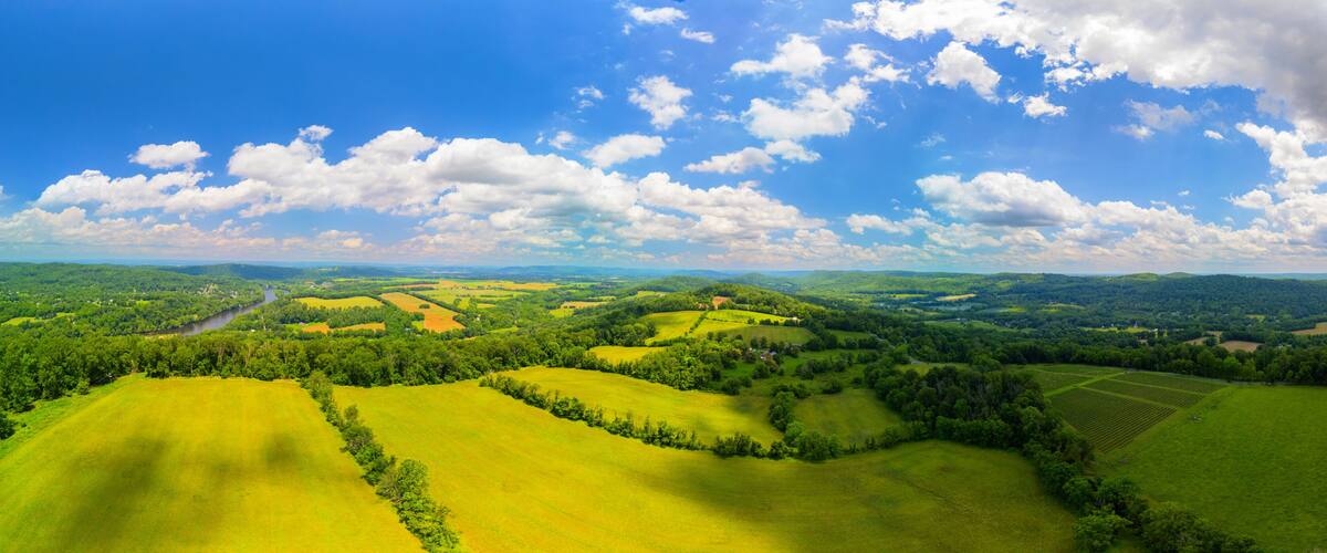 Rolling green hills, a river, and a clear blue sky with clouds.