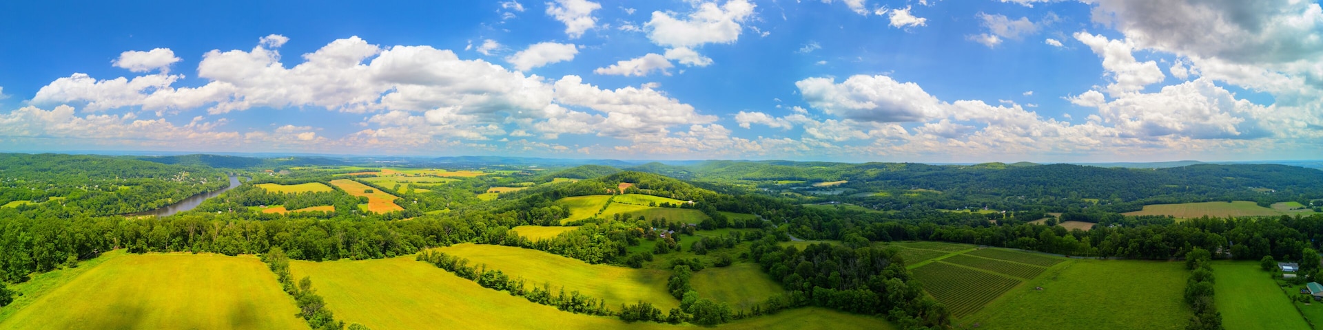 Rolling green hills, a river, and a clear blue sky with clouds.