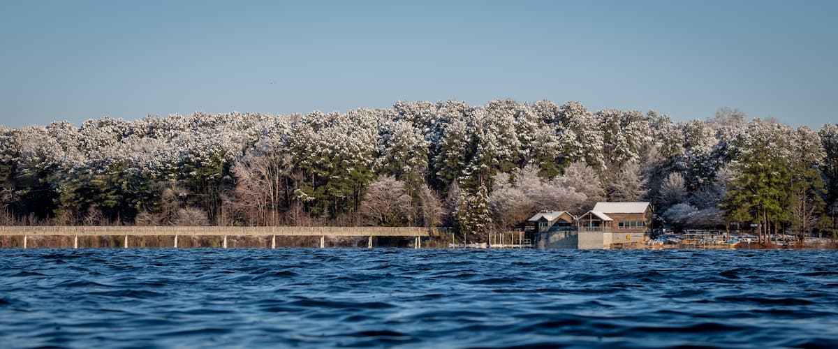 Een waterlichaam met een houten steiger die erin uitstelt, omgeven door met sneeuw bedekte bomen en een heldere lucht.