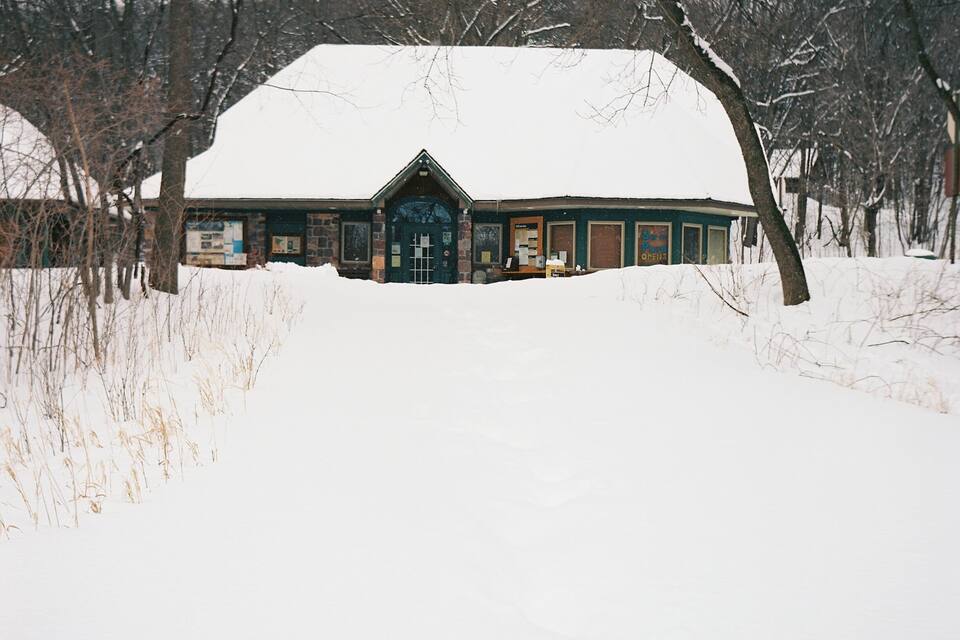 A snow-covered building with a green roof and a sign that reads "Swim the Pond Opens."