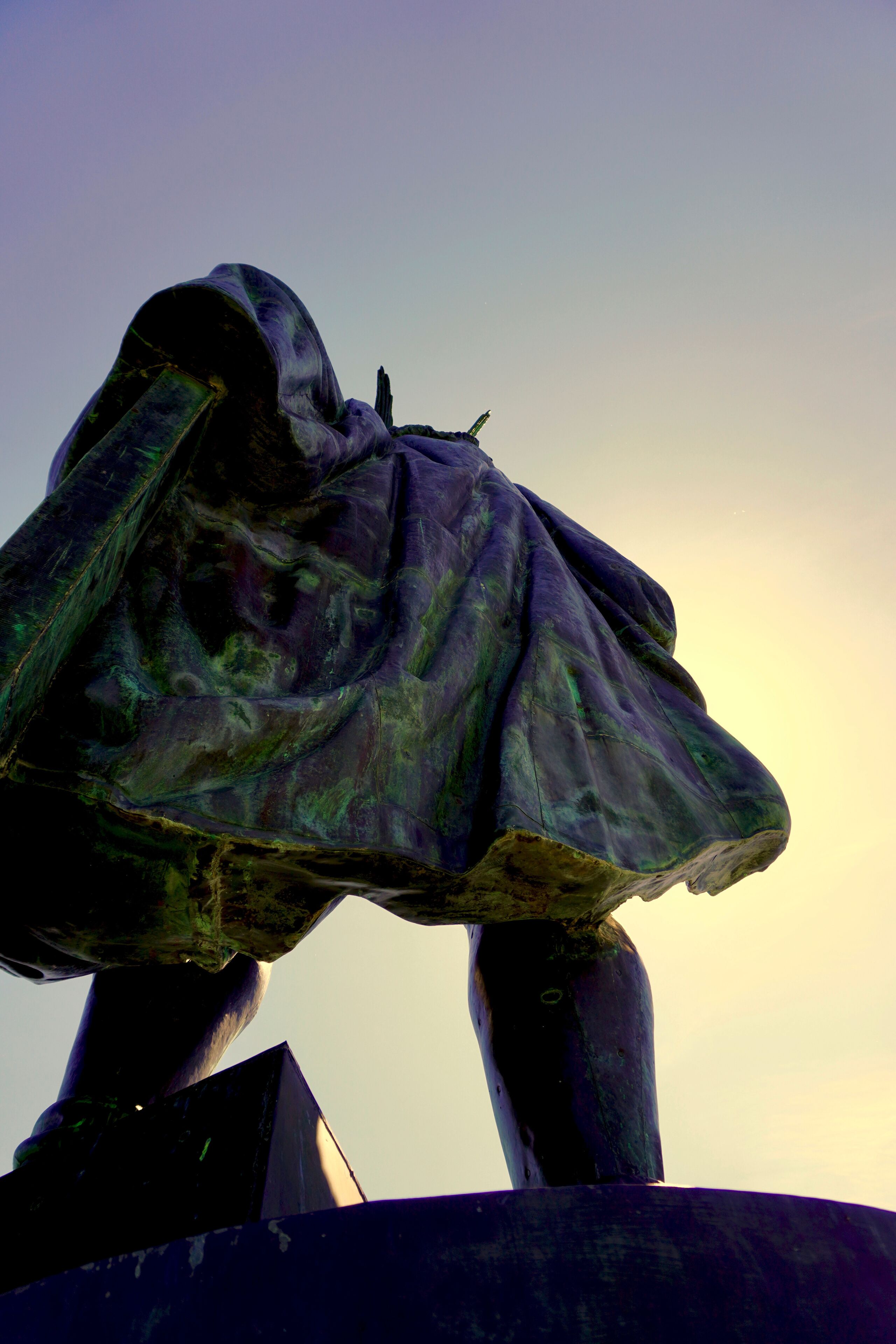 A statue with a flowing garment, set against a clear sky.
