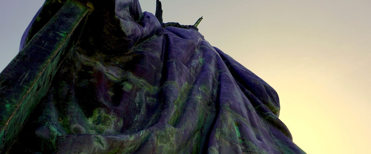 A statue with a flowing garment, set against a clear sky.