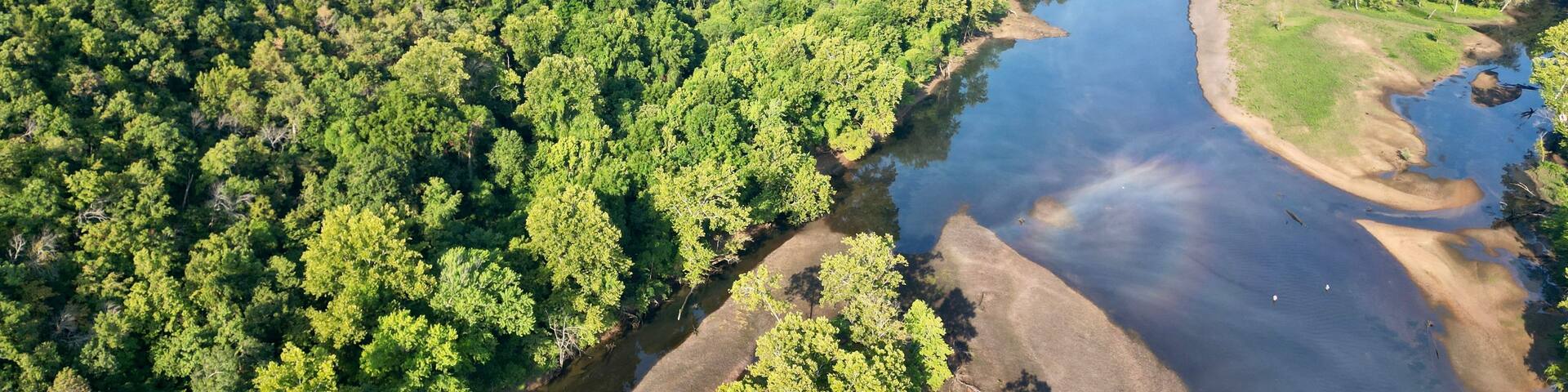 A river winding through a densely forested area with a dam in the distance.