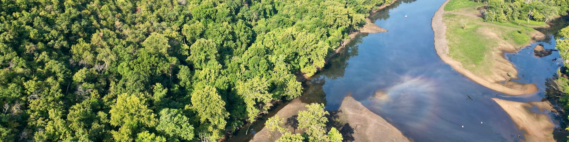 A river winding through a densely forested area with a dam in the distance.