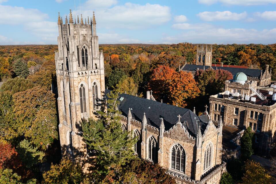 A historic church with a tall tower and a smaller building with a green dome, surrounded by autumn foliage.