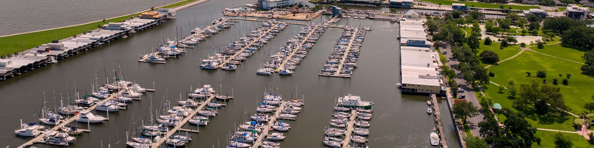 A marina with numerous boats docked, a coastal road, and a sunset sky.