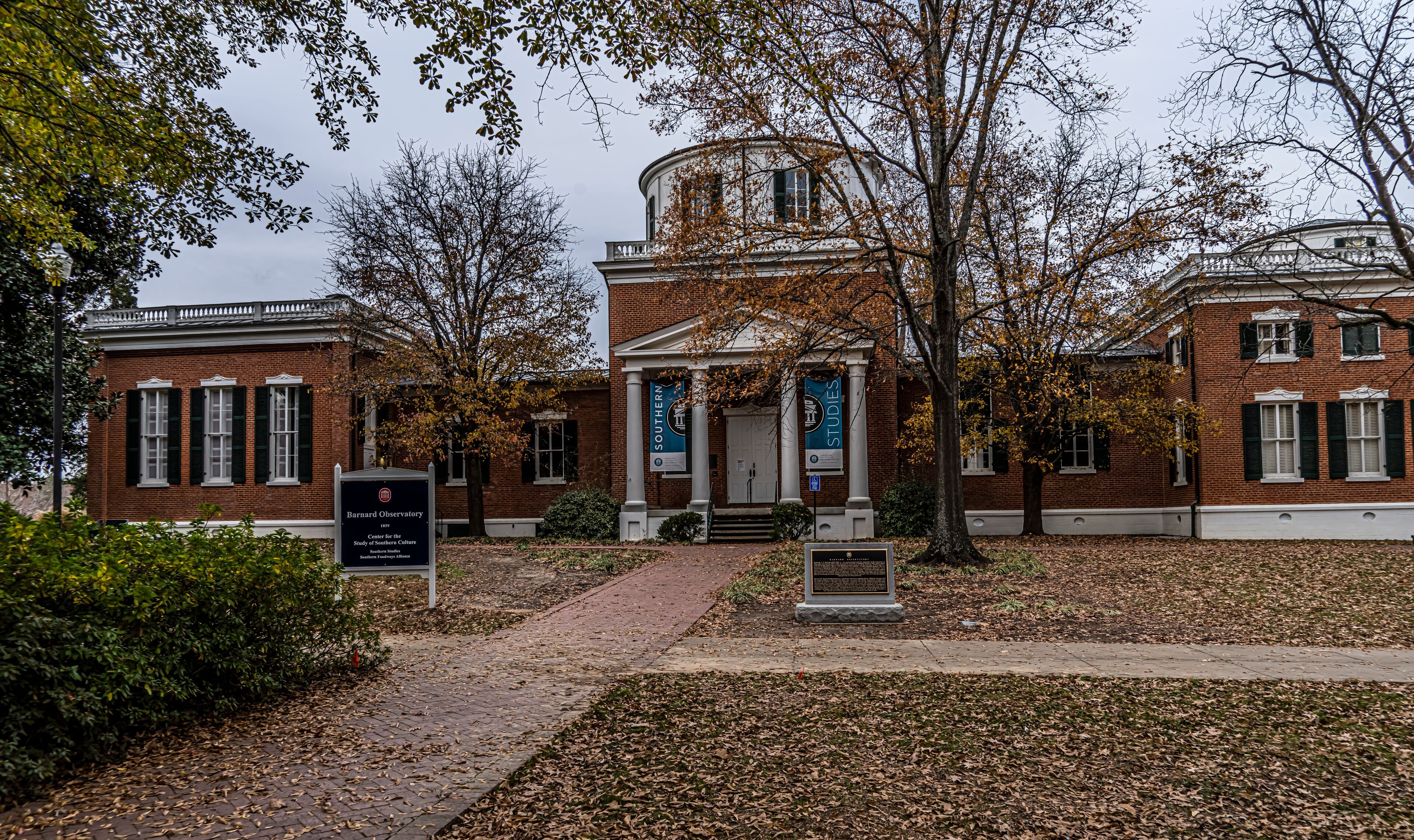 A historic building with a central dome, surrounded by trees and a brick facade.