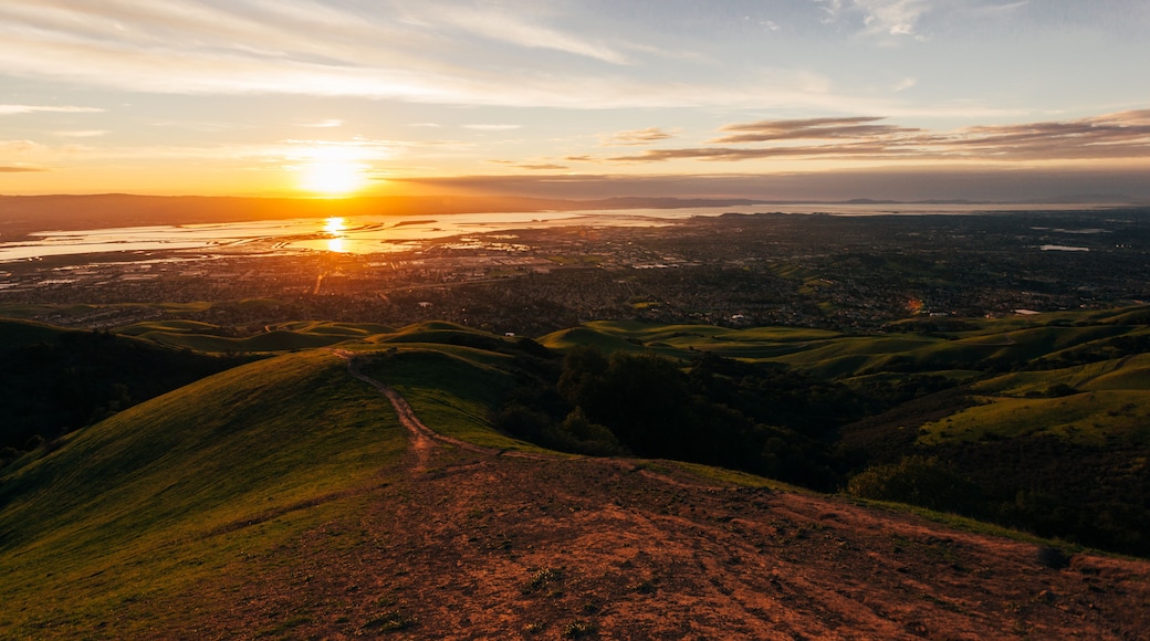 A sunset over a hilly landscape with a river and city in the distance.