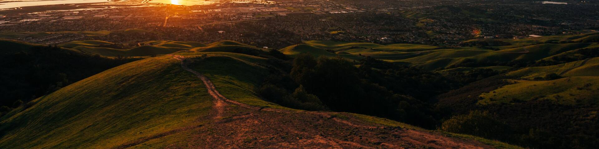 A sunset over a hilly landscape with a river and city in the distance.