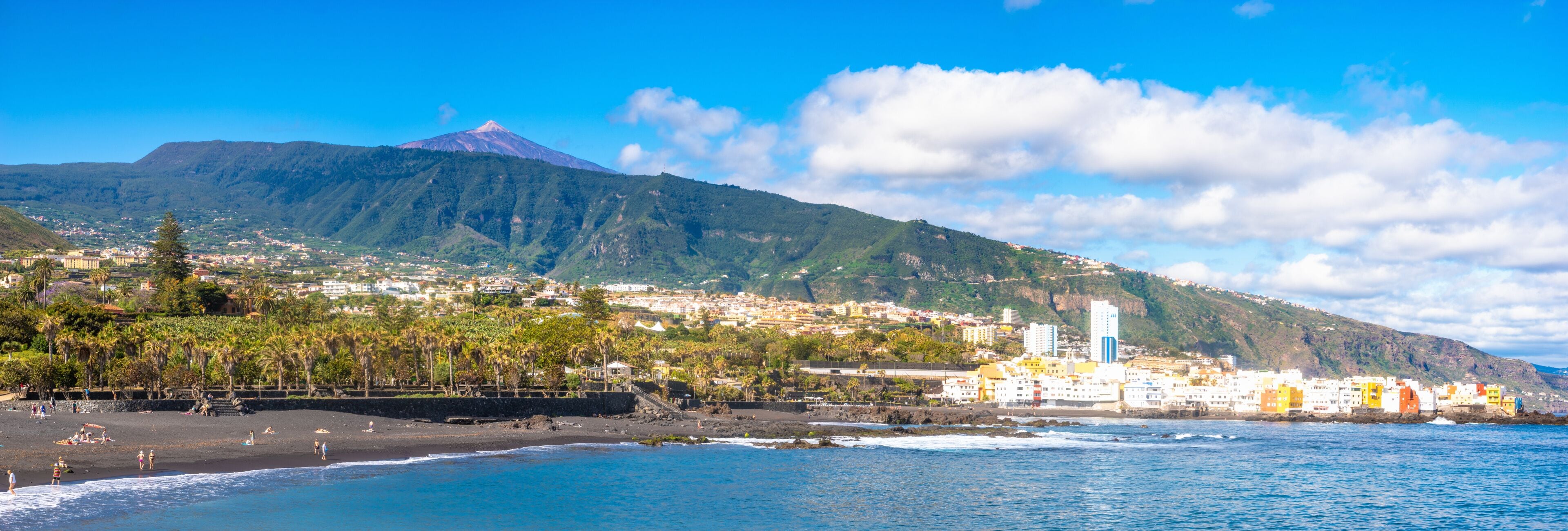 A coastal town with a mountain in the background, a beach, and colorful buildings.