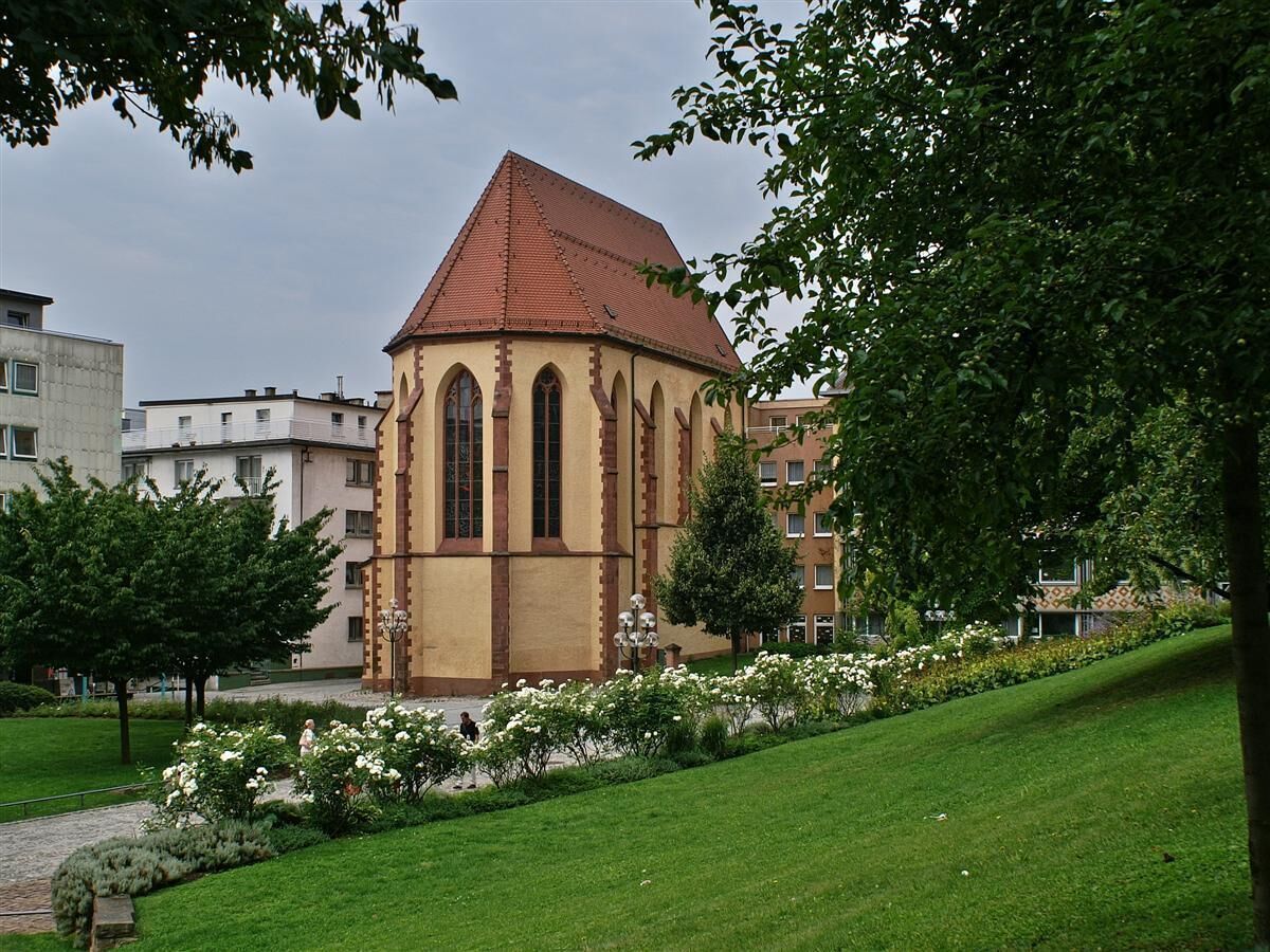 A church with a red roof and arched windows, surrounded by a well-maintained lawn and flowering bushes.