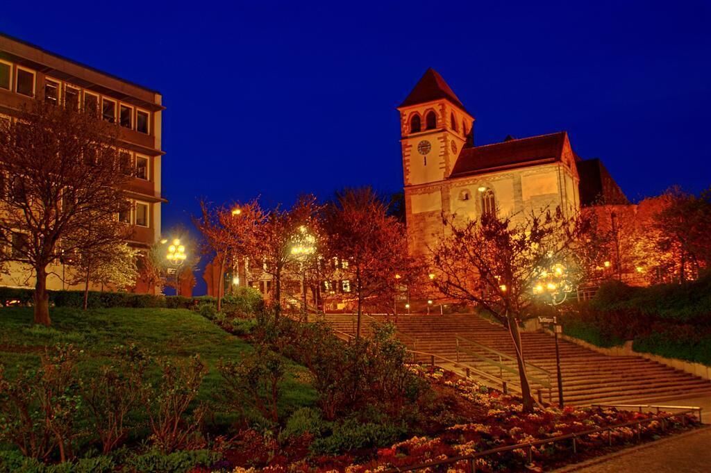 A historic building with a clock tower, surrounded by trees and illuminated by street lamps.