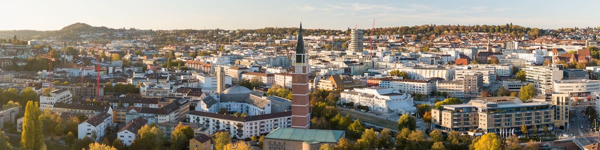 Eine Stadtansicht mit einem markanten Kirchturm, dichter Bebauung und umgebender Grünfläche.