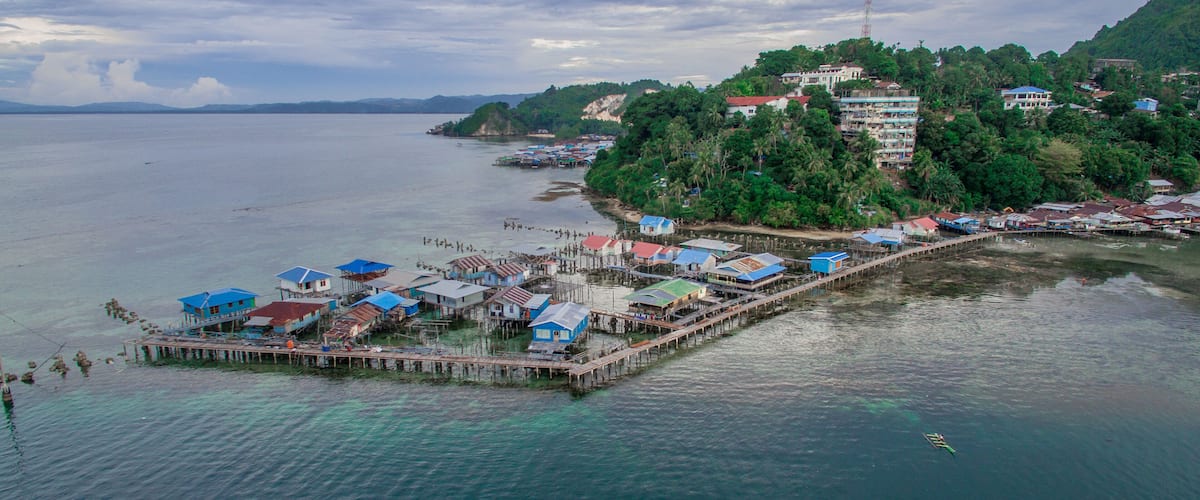 A coastal village with stilt houses, a pier, and a hilltop building.