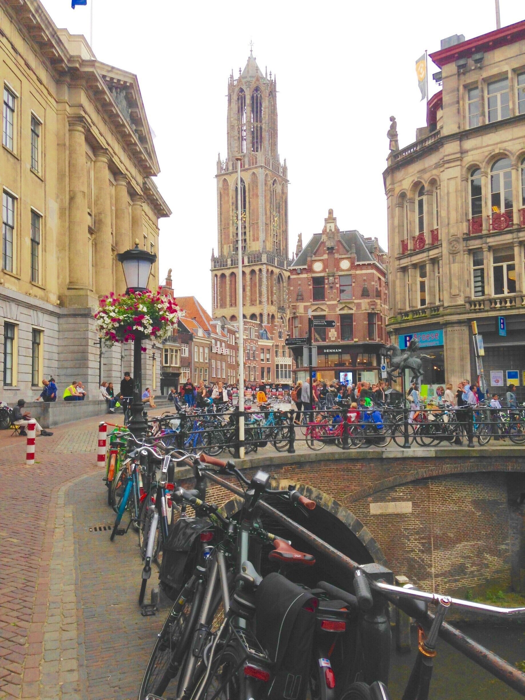 Una plaza histórica de la ciudad con una torre de iglesia destacada, bordeada de bicicletas y peatones.