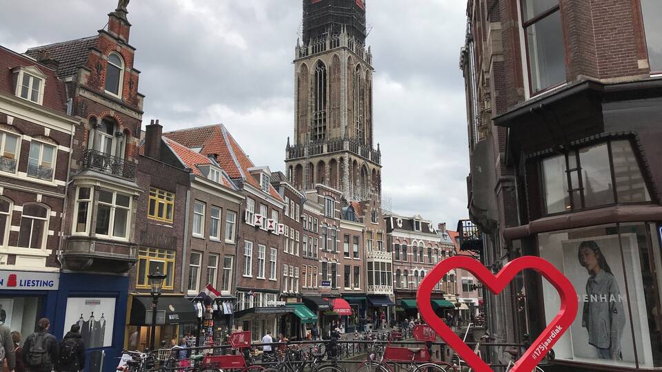 A historic European town with a prominent church tower, traditional buildings, and a red heart-shaped sculpture.