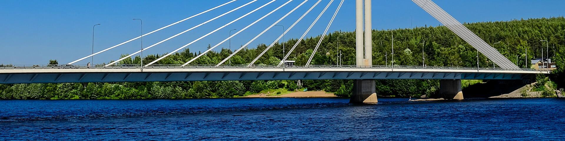 A cable-stayed bridge over a river with a forested hillside in the background.