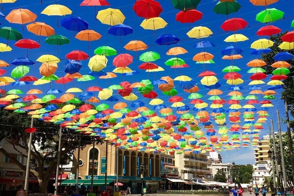 Une place agrémentée de parasols colorés suspendus au plafond.