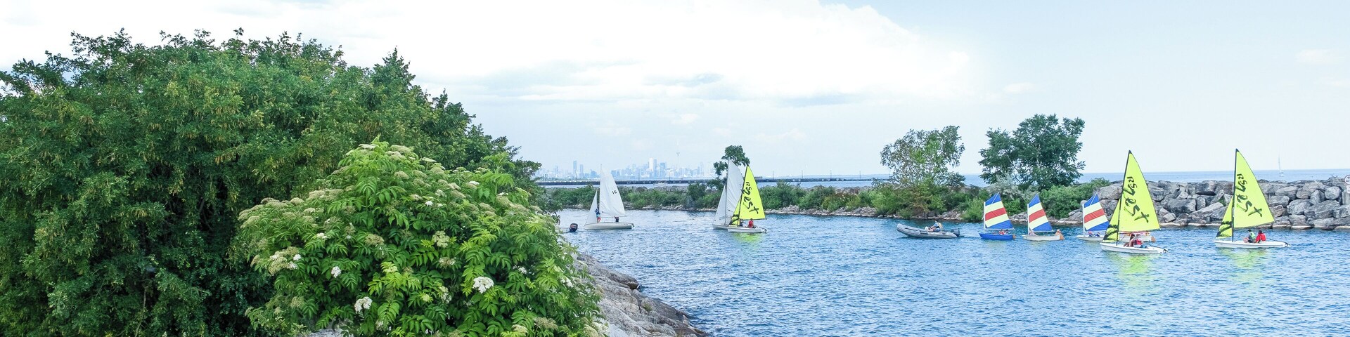 A calm river with sailboats, a rocky shoreline, and lush greenery.