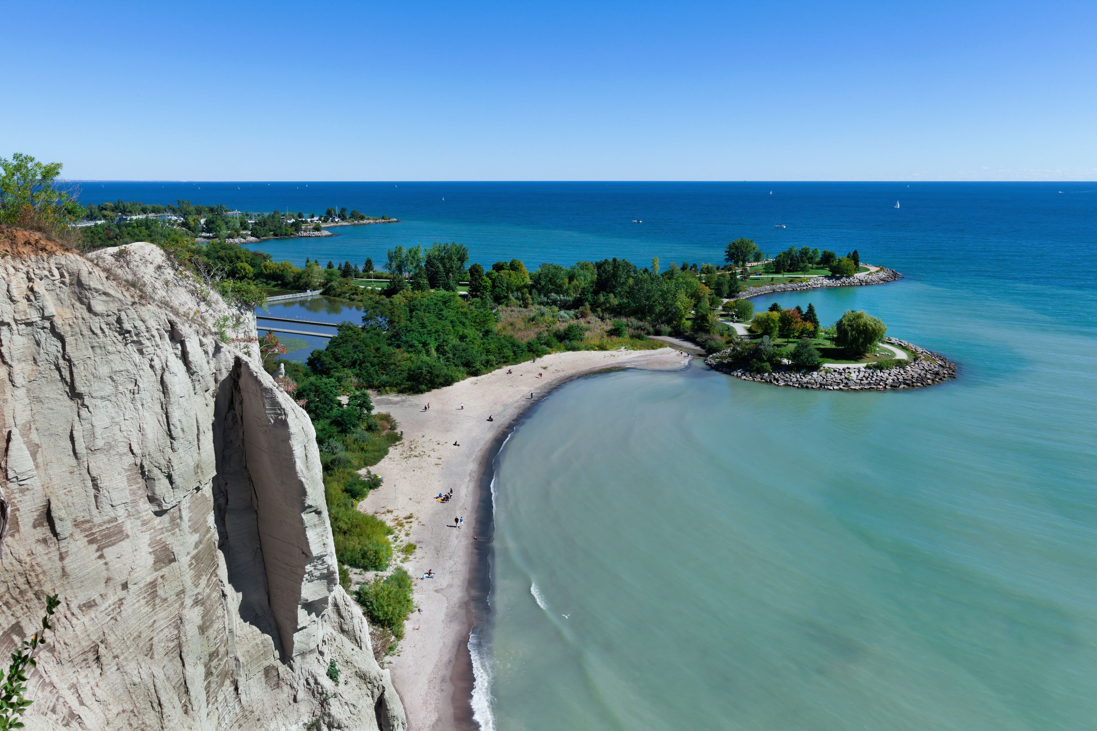 Un paisaje costero con playa arenosa, acantilado rocoso y mar tranquilo.