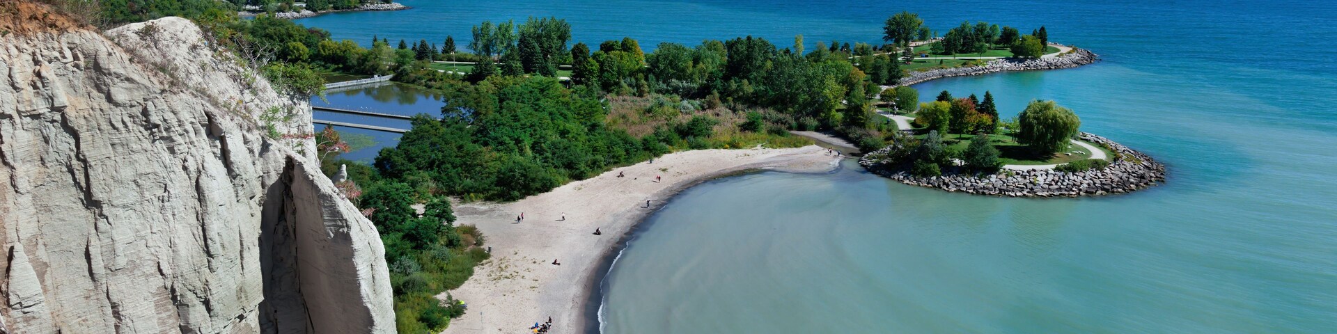 Un paisaje costero con playa arenosa, acantilado rocoso y mar tranquilo.