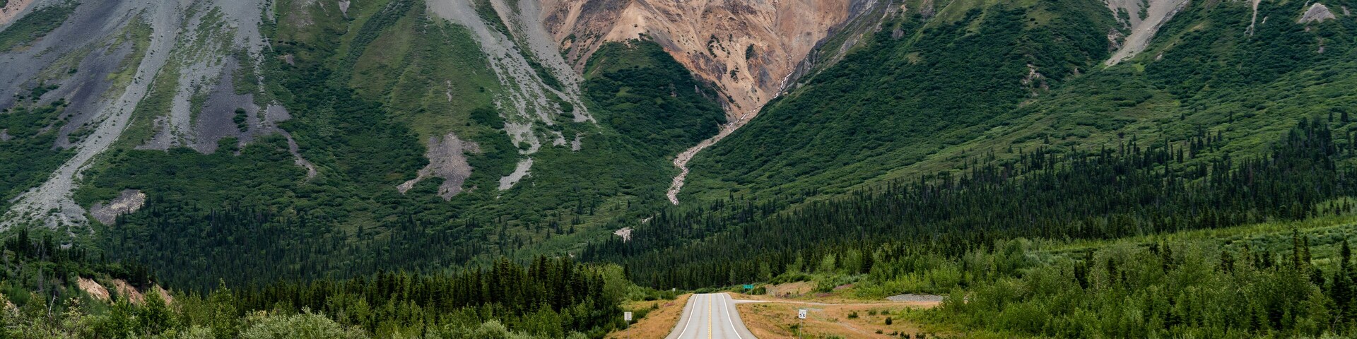 Uma estrada serpenteando por uma paisagem montanhosa com vegetação exuberante e falésias rochosas.