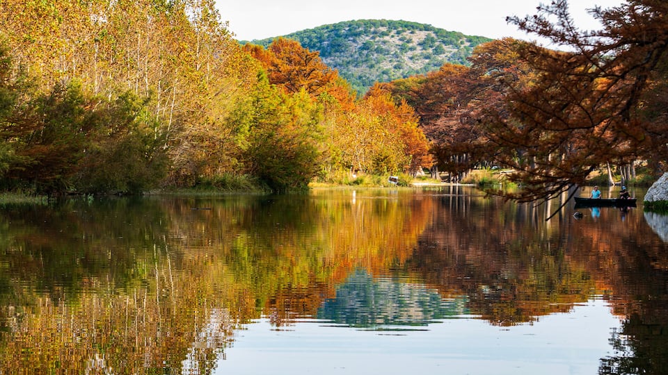 A calm lake surrounded by autumn-colored trees and a distant hill.