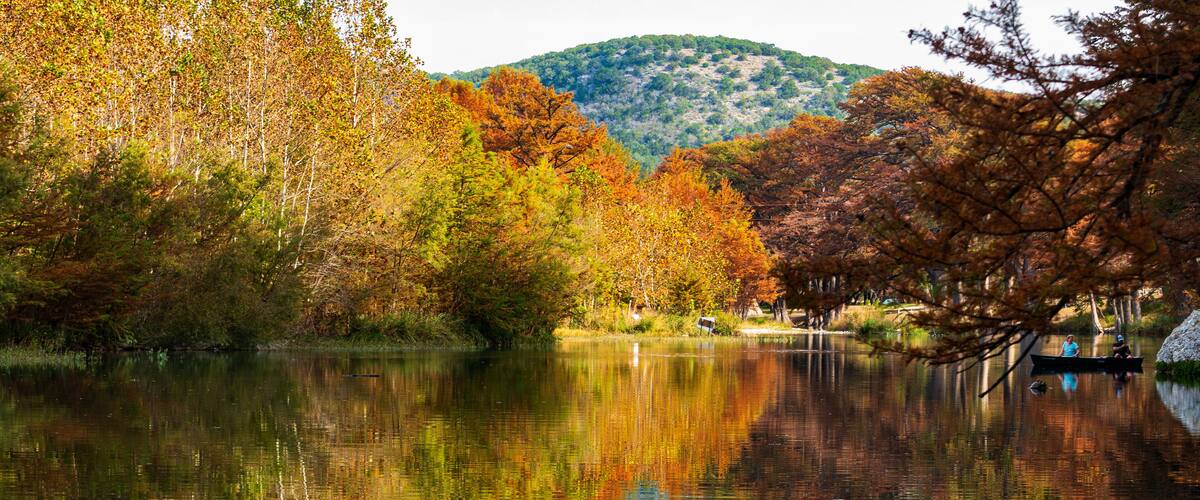 A calm lake surrounded by autumn-colored trees and a distant hill.
