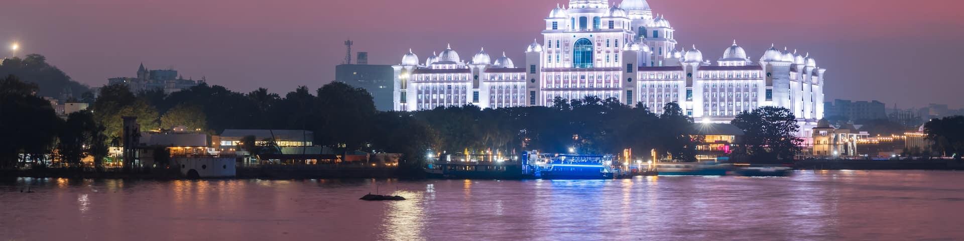 A grand illuminated building with domes by a river at night.